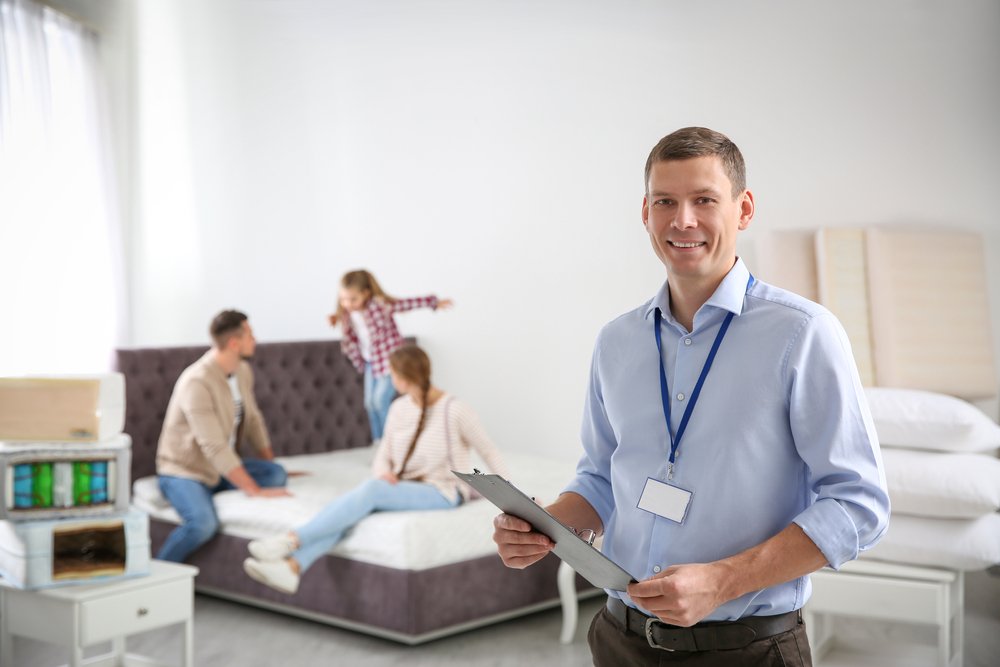 Happy,Salesman,And,His,Clients,In,Mattress,Store